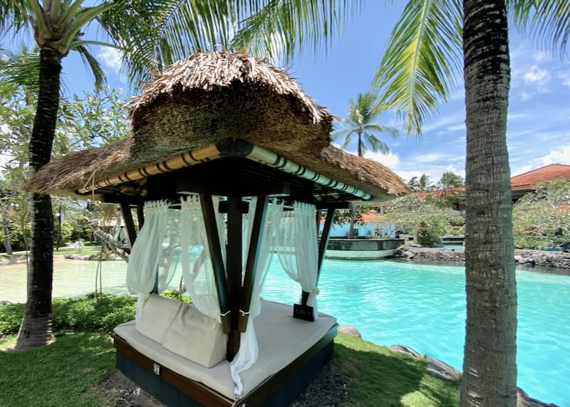 A hut with sheer drapes sits next to the lagoon at The Laguna Luxury Collection Resort & Spa in Nusa Dua Bali.