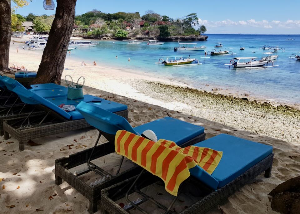 Blue Hai Tide hotel lounge chairs lay on beach while boats sits on Mushroom Bay.
