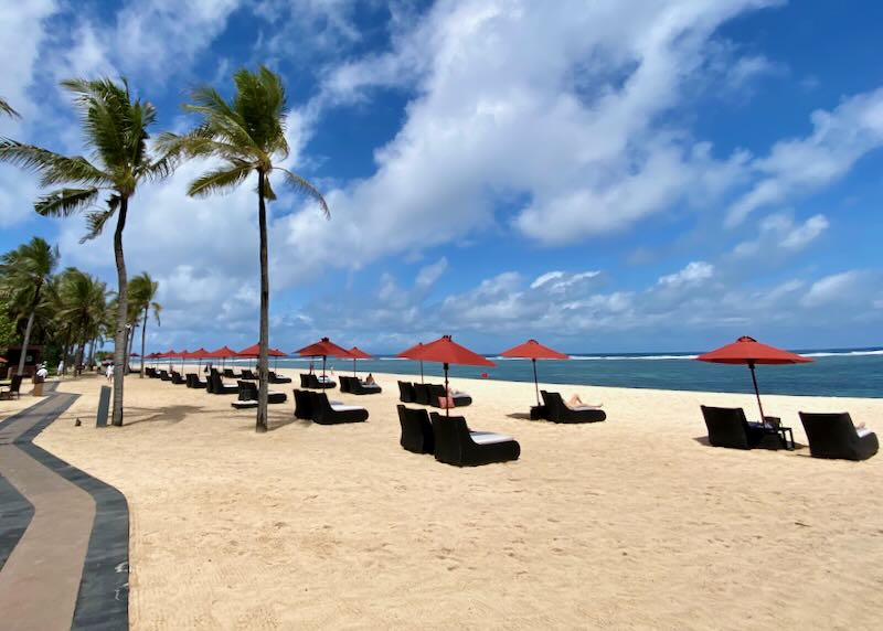 White sand beach with lounge chairs at St. Regis Resort in Nusa Dua Bali.