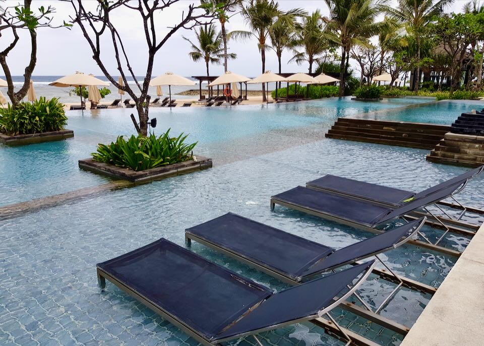 Lounge chairs sit in a pool by the ocean.