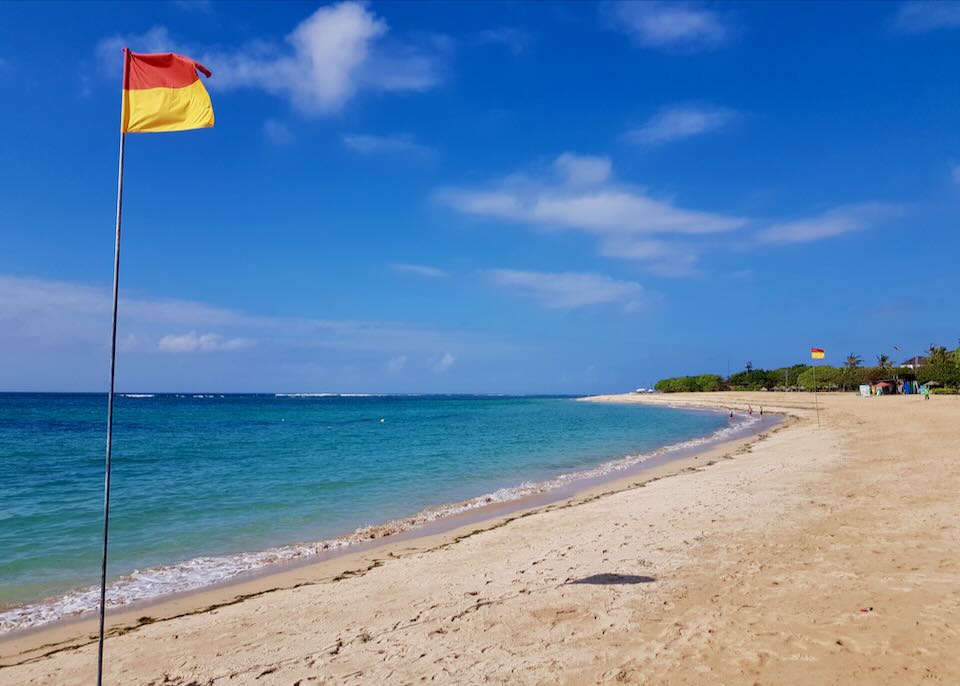Beachfront with white sand and a flags.