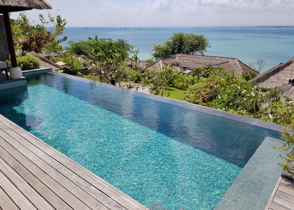 An infinity pool with a wood deck overlooks the roofs of other villas and the bay.