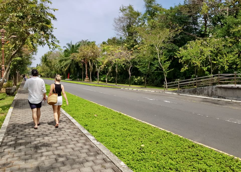 A couple walks on a sidewalk next to the road.