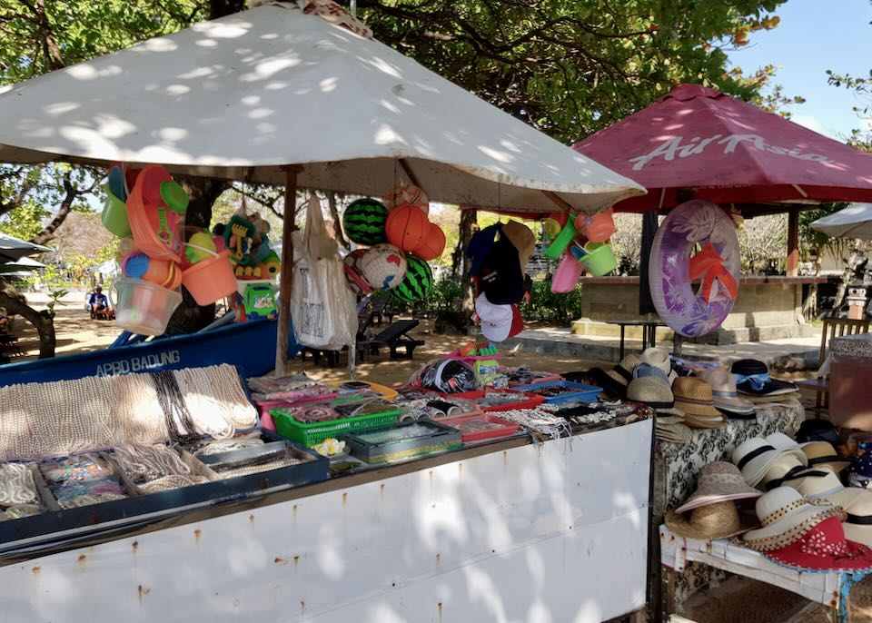 A vender stands with hats and beach items.