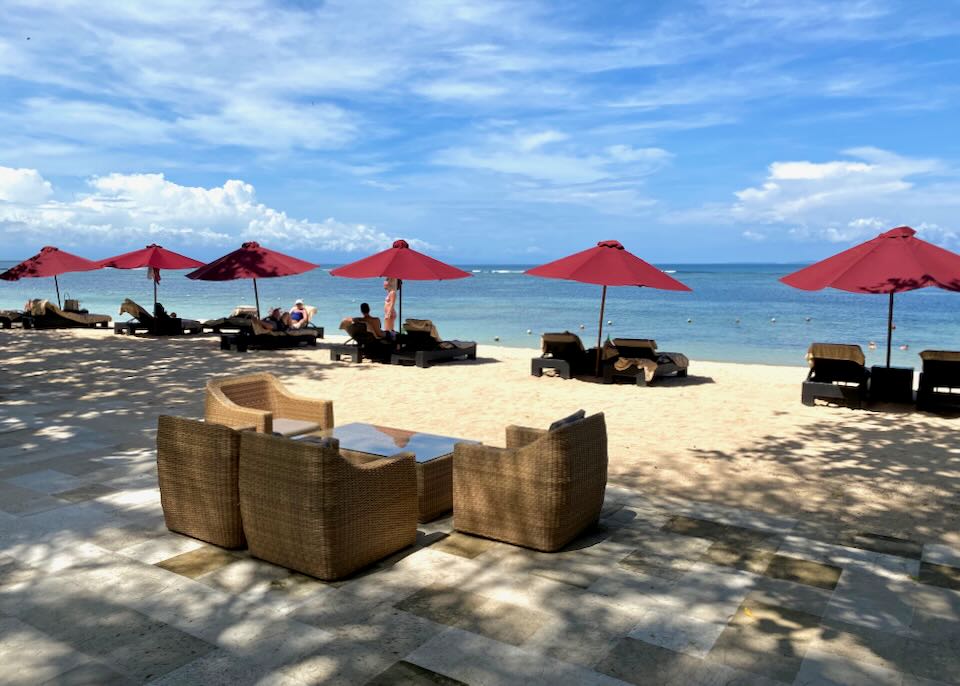 Guests lounge on the beach under red umbrellas.