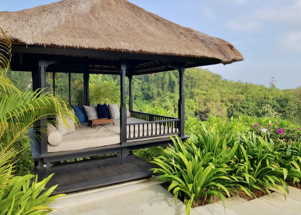 A thatched roof gazebo with pillows and cream mattresses overlooks the jungle and beach.