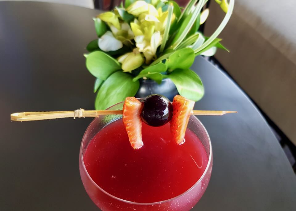 A glass filled with a red drink and fruit spear sit on a table.