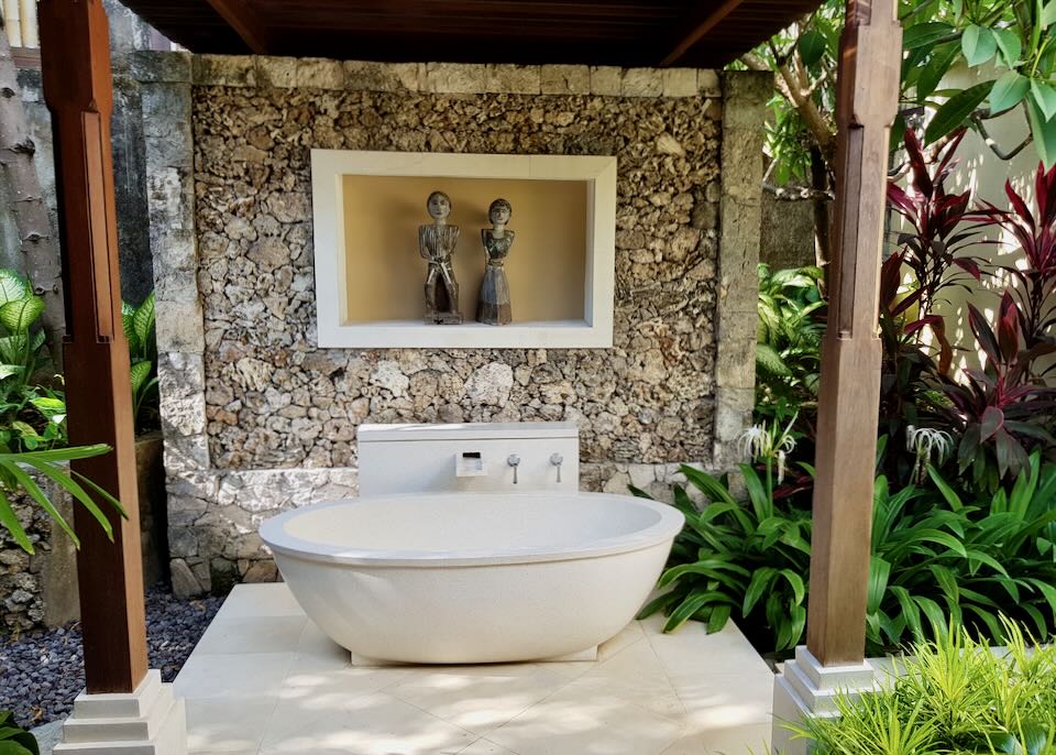A white tub sits on white tile outdoor surrounded by plants.