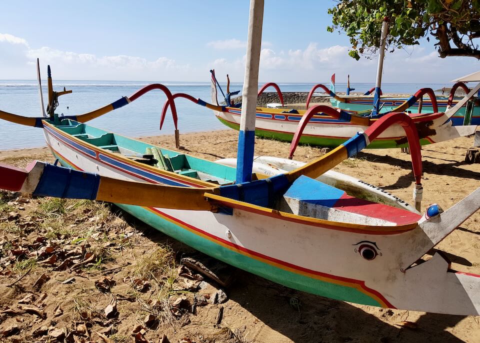 A colorful Jukung boat sits in the sand on the beach waiting to go on the water.