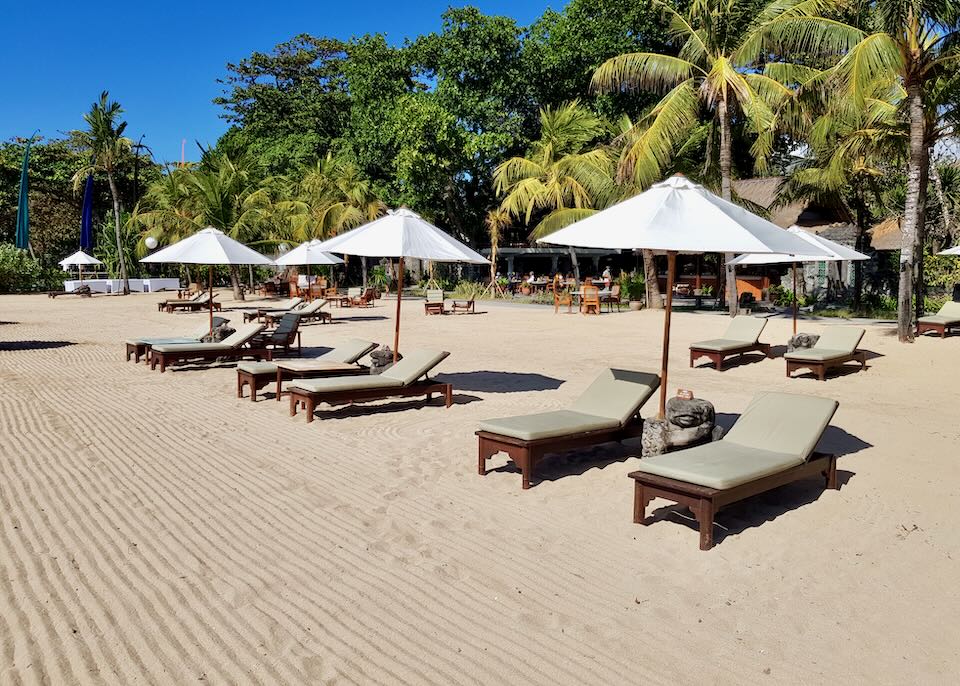Tan lounge chairs sit on the beach under umbrellas.