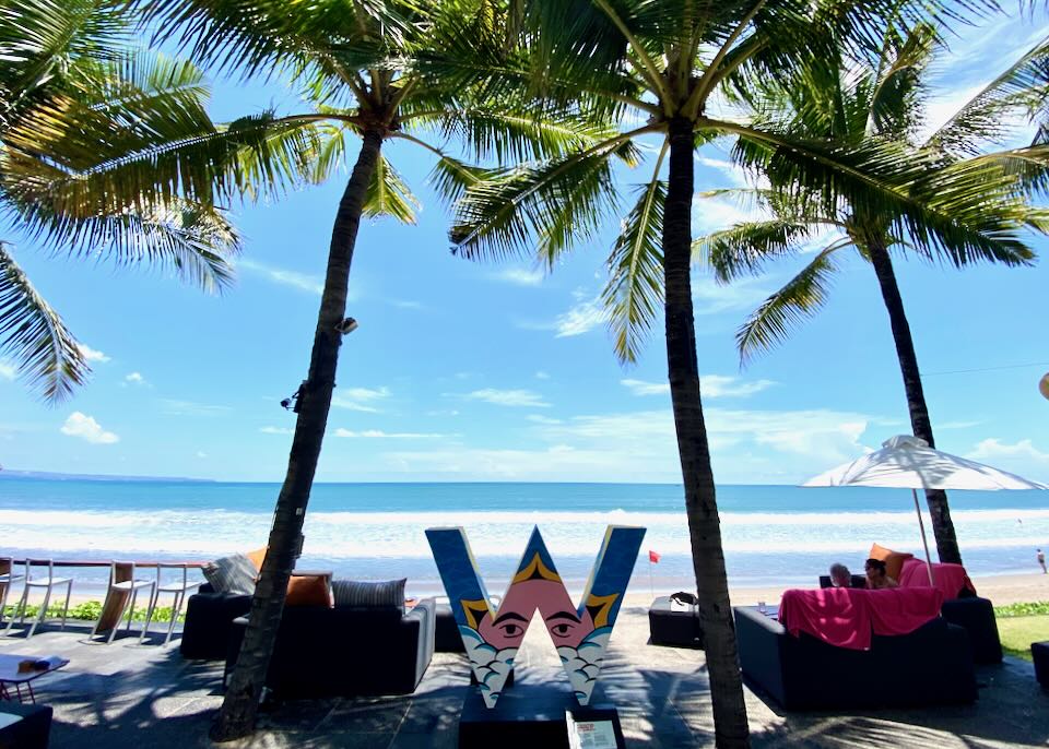 A single "W" painted with a face sits under palm trees by the beach.