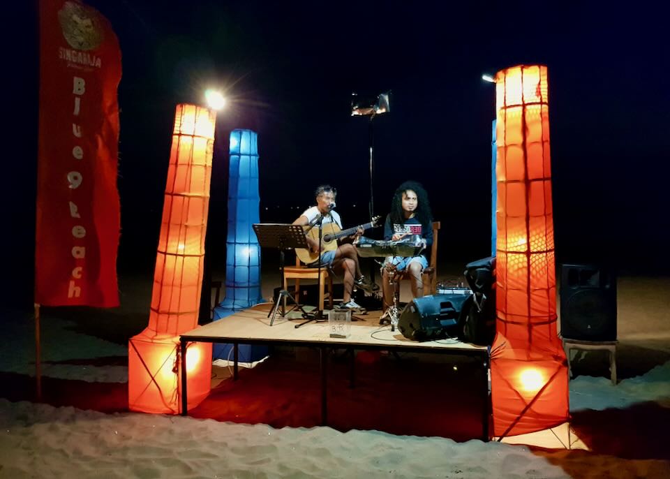 Two musicians play on a stage set on the beach.