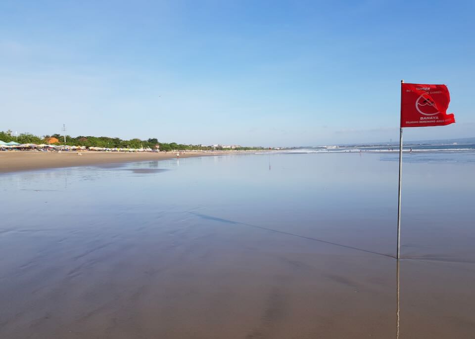 A red flag on a beach blows in the wind.