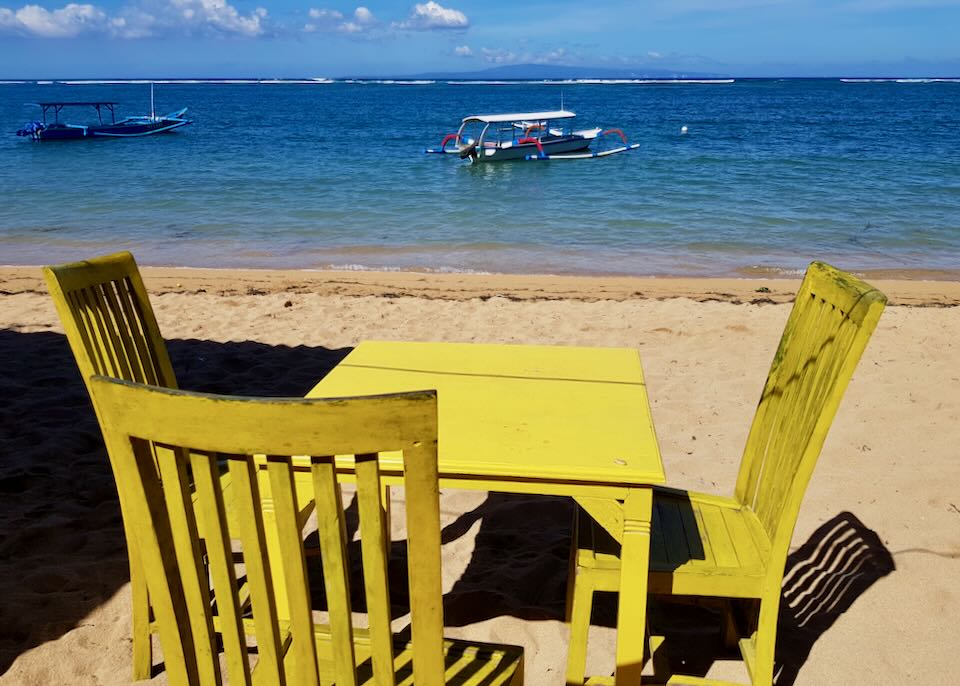 A bright yellow table and chairs sit on the beach.