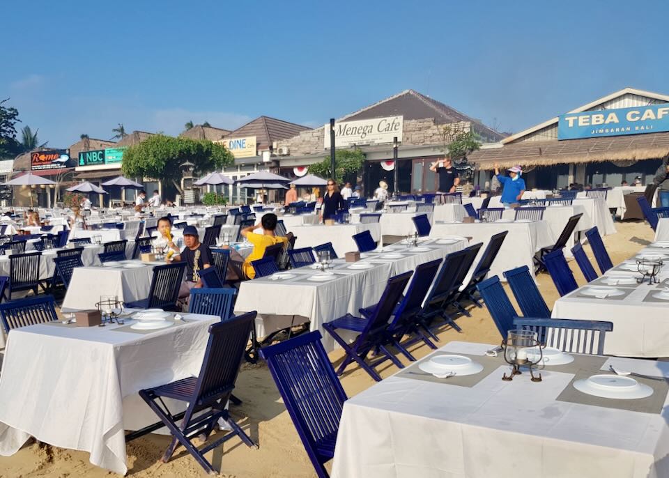 Dozens of tables and chairs sit on the beach.