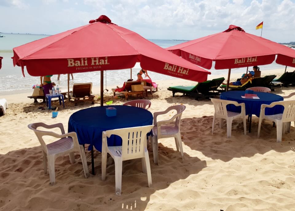 A few plastic tables with red umbrellas sit on the beach.