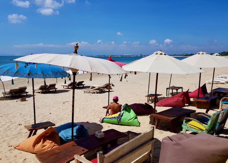 People lounge on colorful beanbags in the sun on the beach.