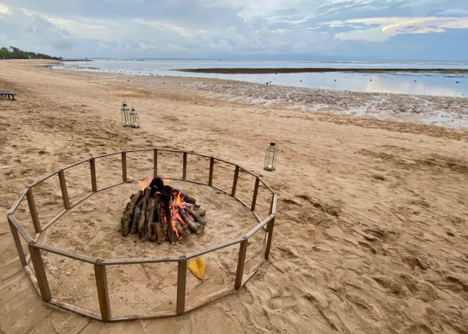 A protected bon fire sits on the beach.