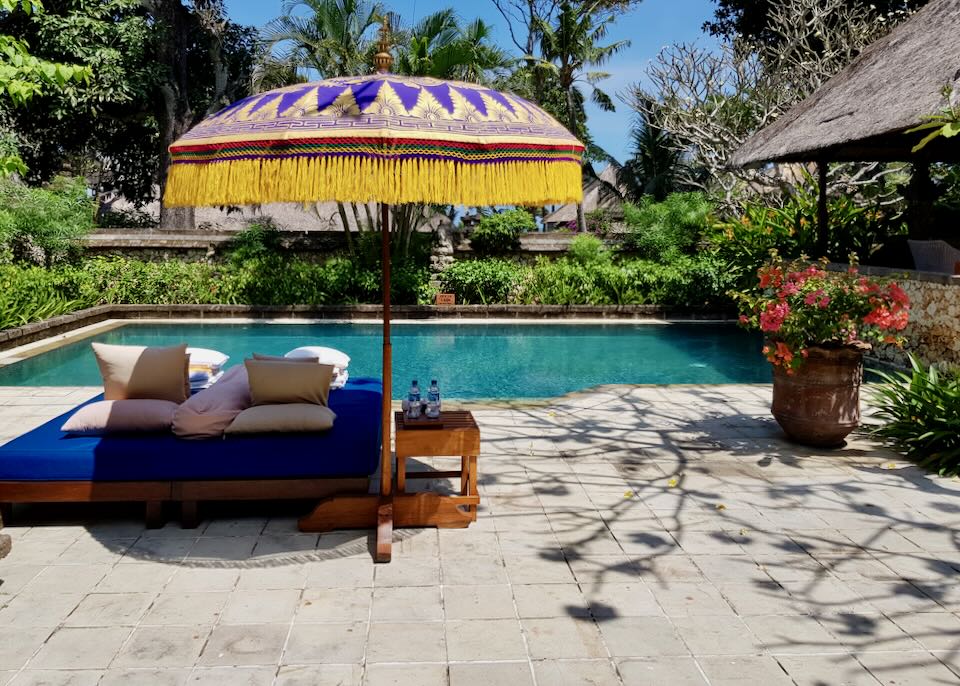 A blue lounge chair and umbrella sit by a private pool at a villa.