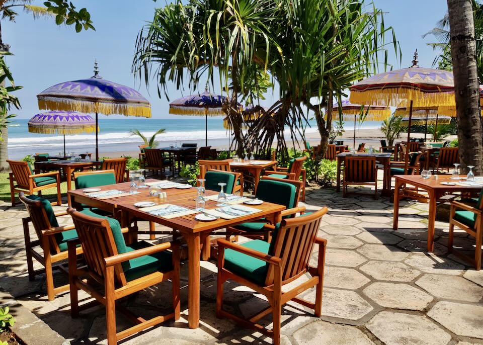 Chairs and tables sit on a patio by the beach.