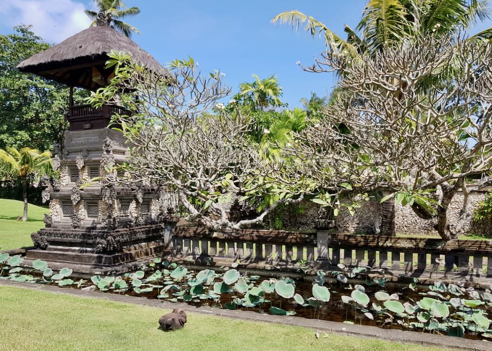 A stone temple sits on a lawn next to a lily pond.