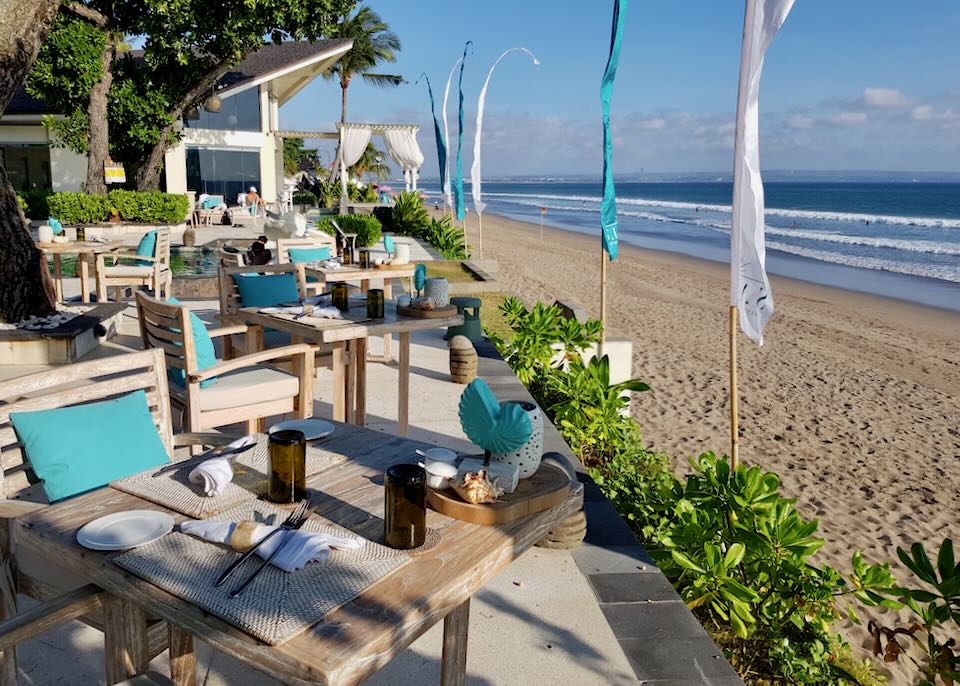 Diner tables and chairs line a patio next to the beach.