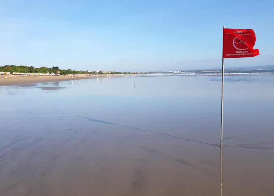 A red flag blows in the wind on the beach.