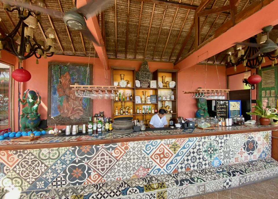A bartender prepares drinks behind a multi-colored tiled bar.