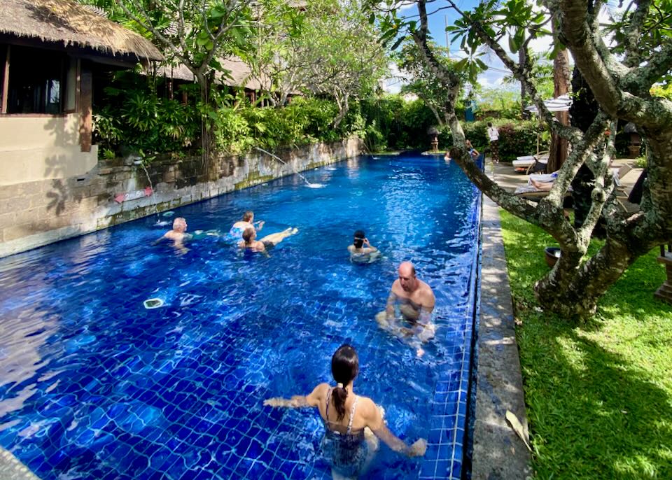 Several guests swim in a bright blue pool.