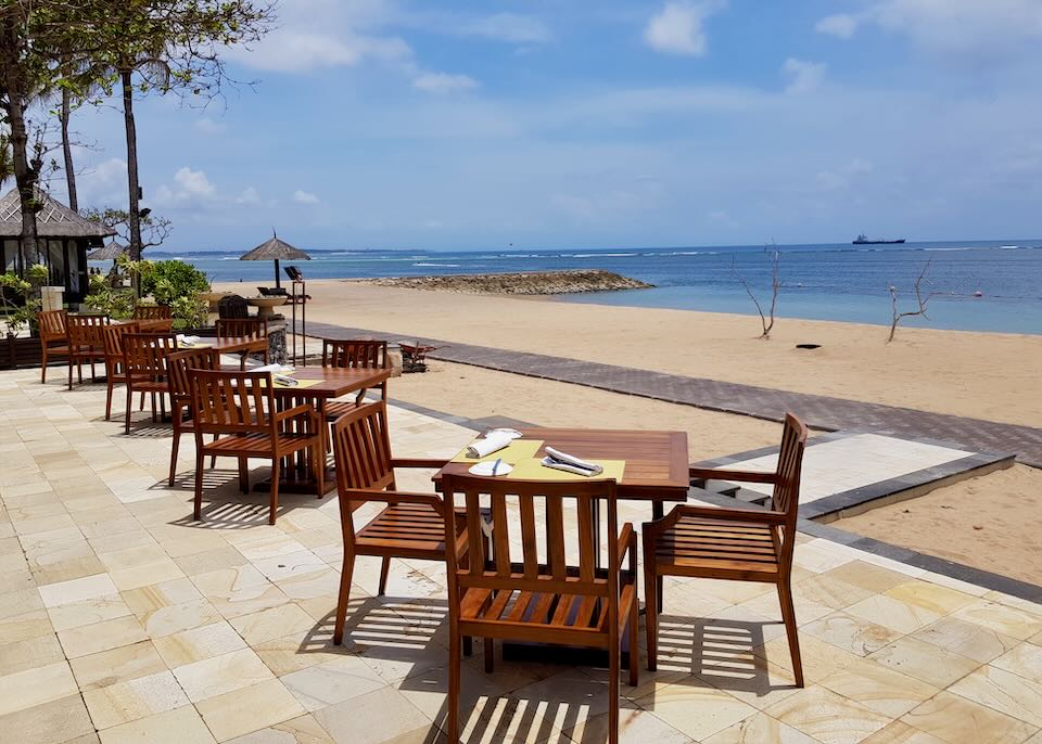 Several tables sit by the beach on a stone patio.