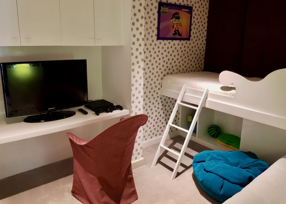 A children's bedroom with an elevated bed and ladder and tv.