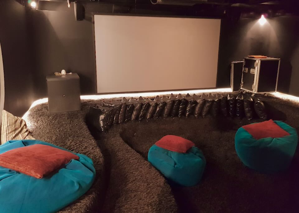 Bean bags sit on a dark carpeted floor in a small movie theater.