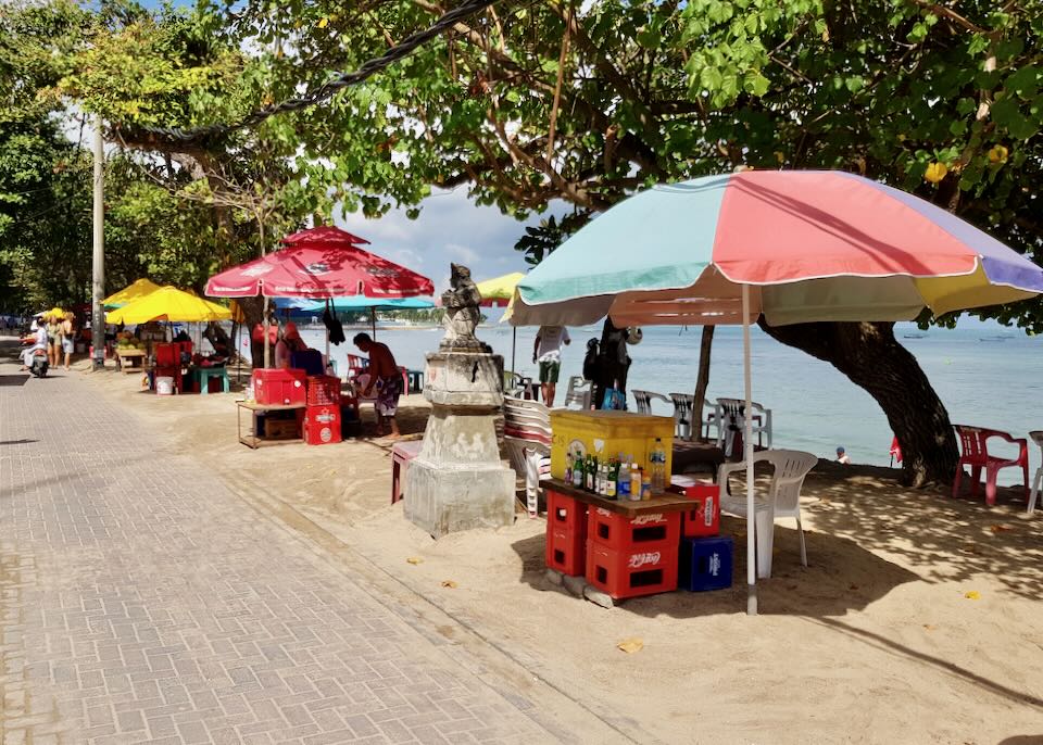 On the side of the road up from the sandy beach, venders selling drinks sit under large umbrellas.