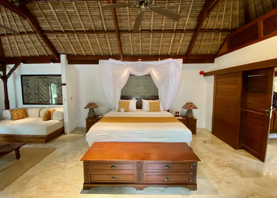 A bed in the center of the room under a thatched roof.