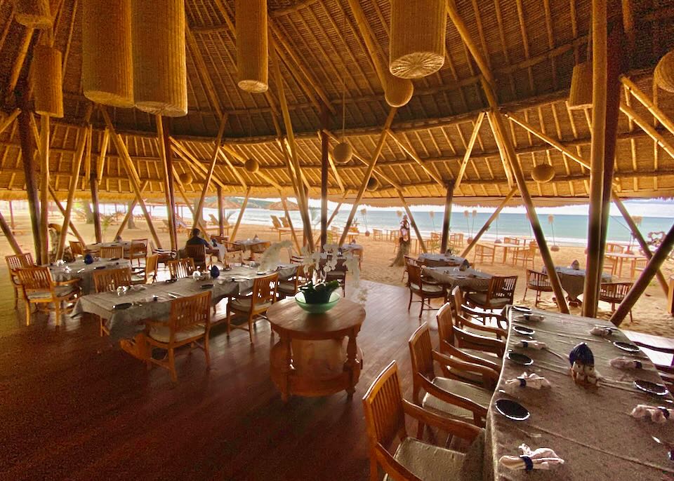 An open-air restaurant under a thatched roof by the beach.