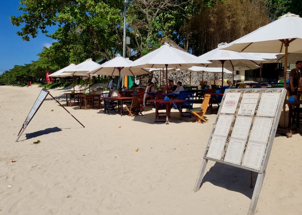 Tables sit on the beach under umbrellas in the sand.