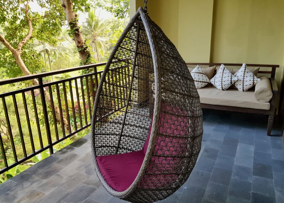 A round wicker swinging chair hangs on a porch.