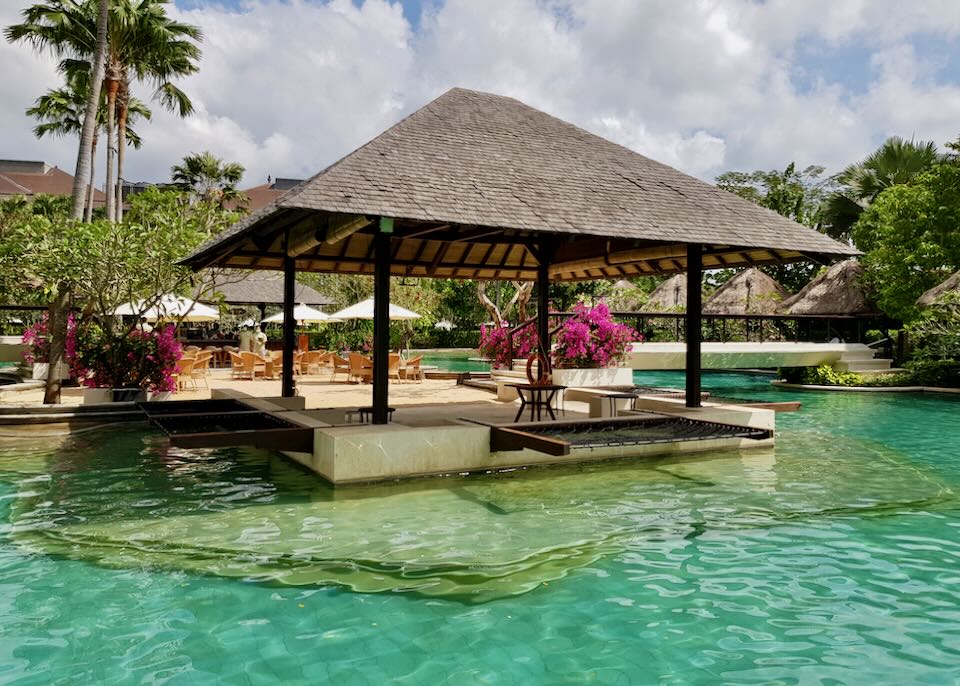A cabana and a pile of sand sit on an island in the middle of the pool.
