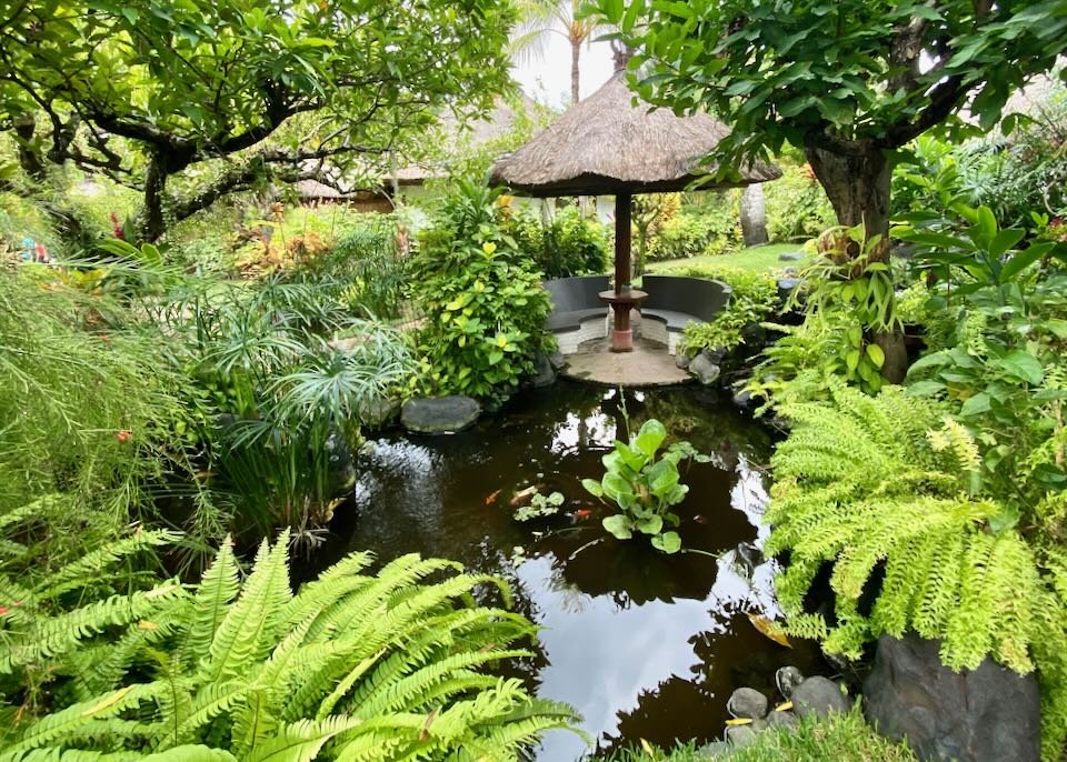 A lush pond with a small covered table and chairs.