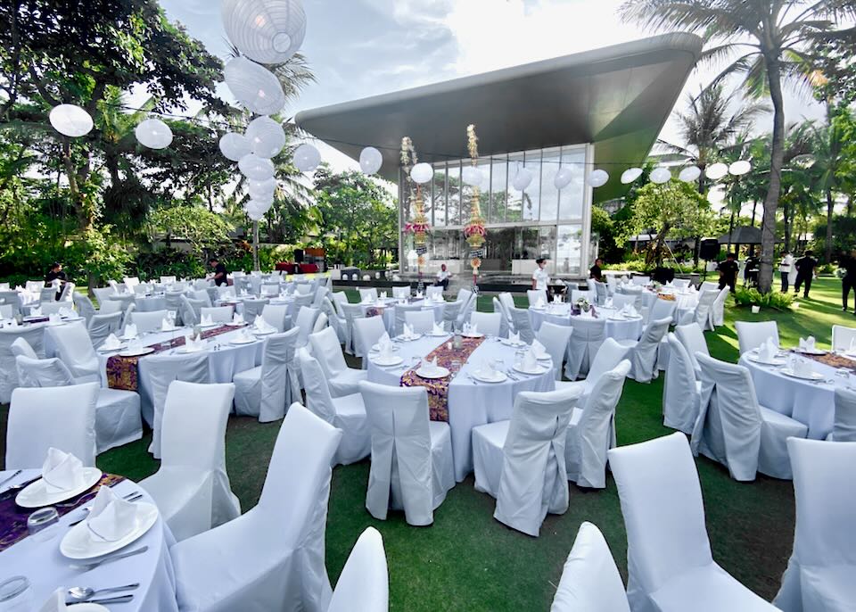 White cloth covered chairs and tables sit on a lawn for a celebration.