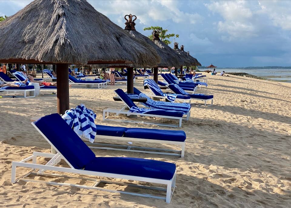 Bright blue lounge chairs sit by the ocean.