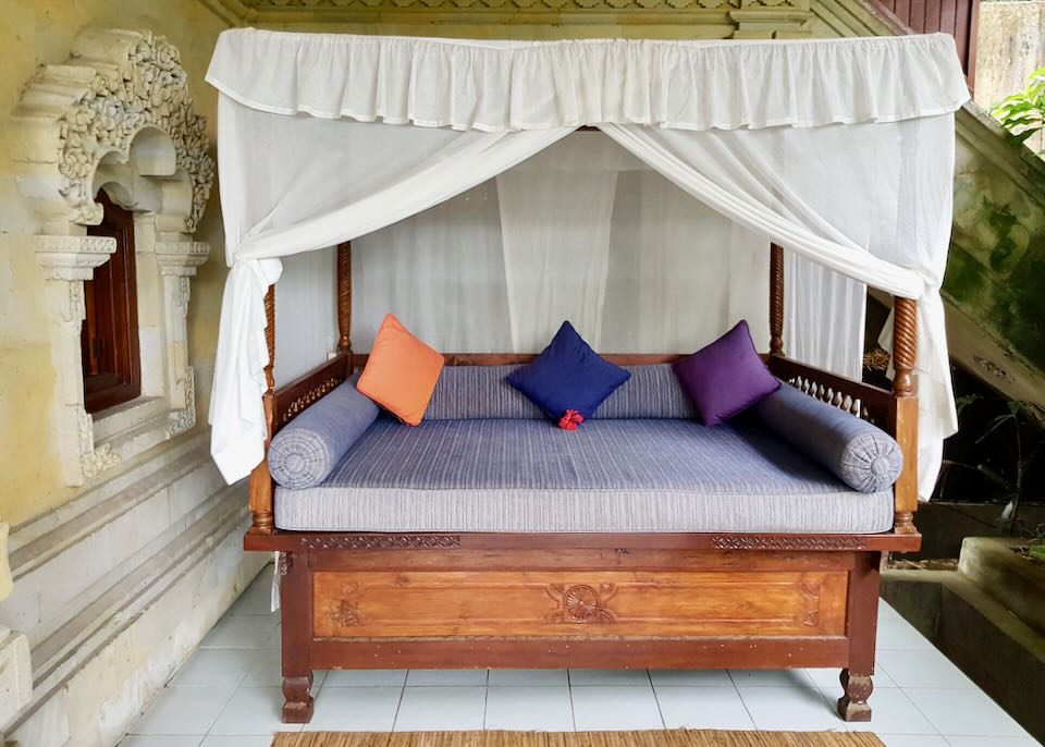 A wood-carved daybed and canopy sit on a balcony.