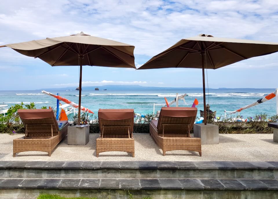 Three lounge chairs sit under umbrellas on the beach.