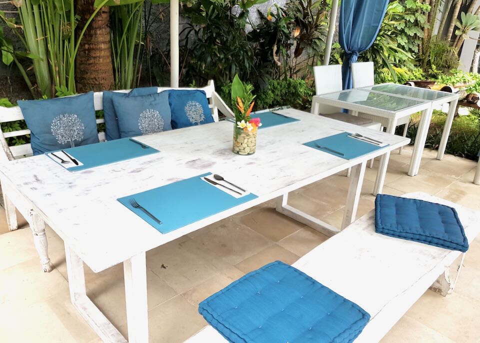 A long white table with blue place mats and pillows.
