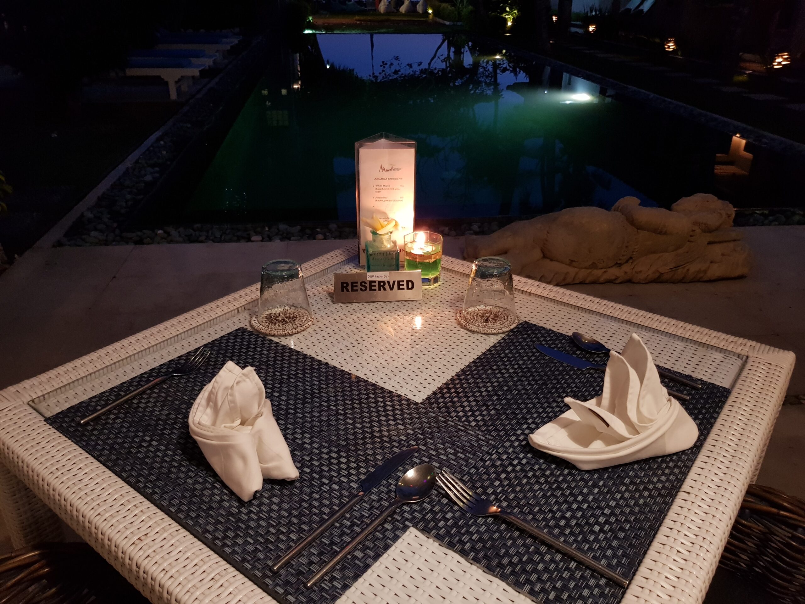 A white whicker table sits by the pool at night.