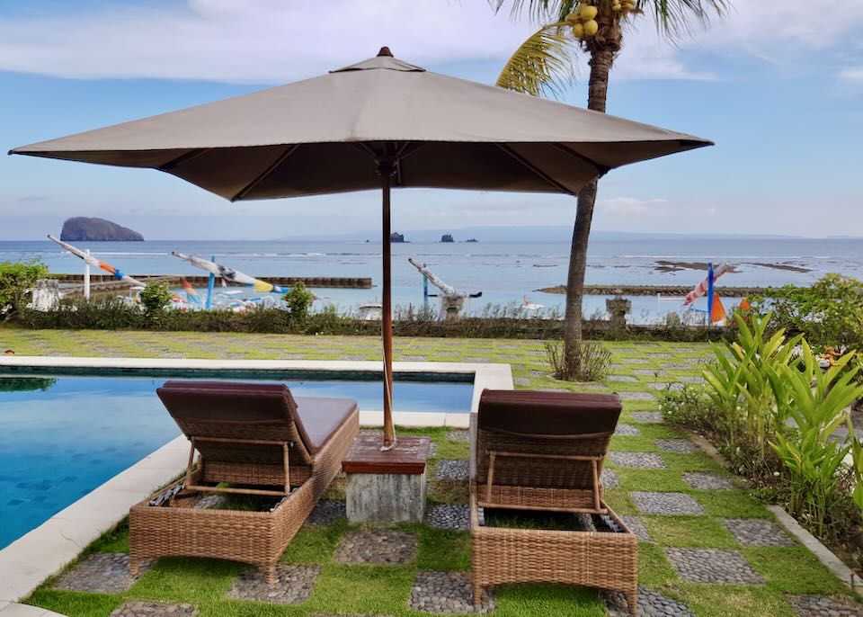 Two lounge chairs sit by the pool and face the sea.