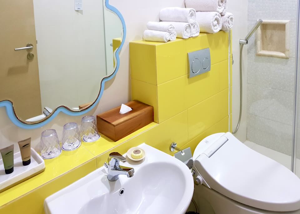 A sink and toilet sit in a yellow tiled bathroom.