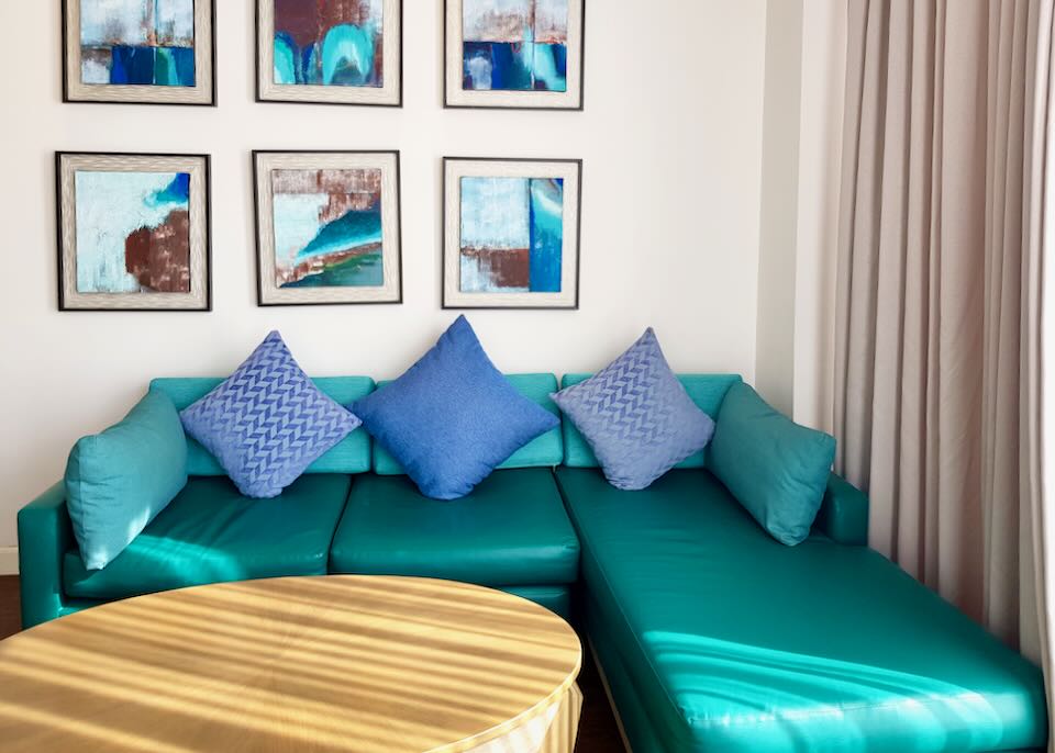A teal sofa and natural wood table sit under 6 framed art pieces.
