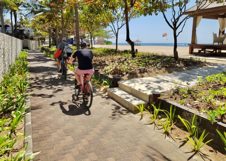 Two people ride their bikes on a stone beach path.