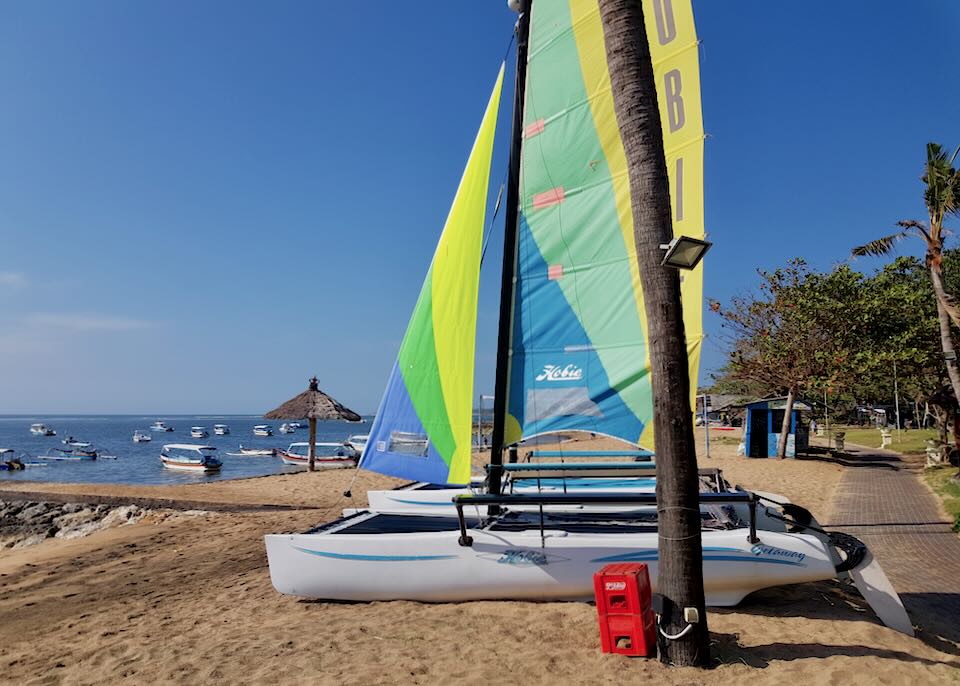 A couple catamaran boats with bright yellow, blue, and green sails sit on the beach.